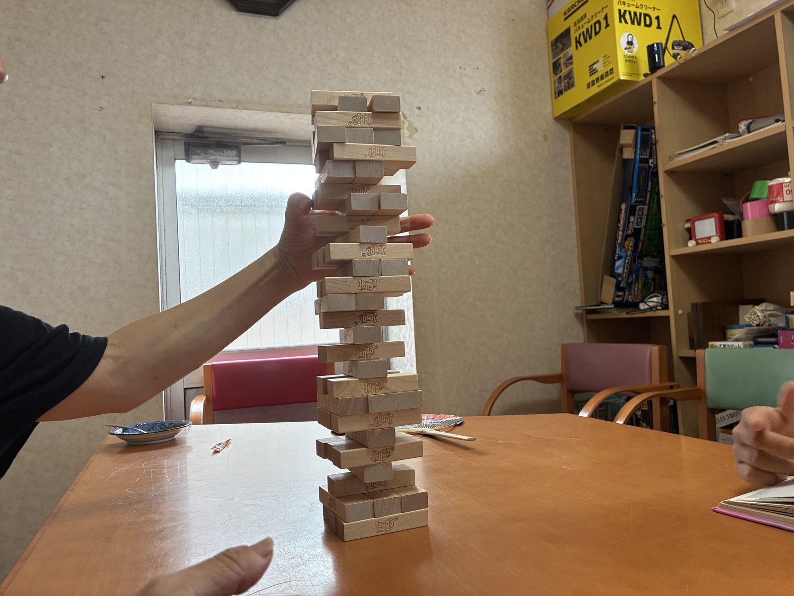 テーブルの上に高く積み上がったジェンガのタワーを、子どもが崩さないように支えている